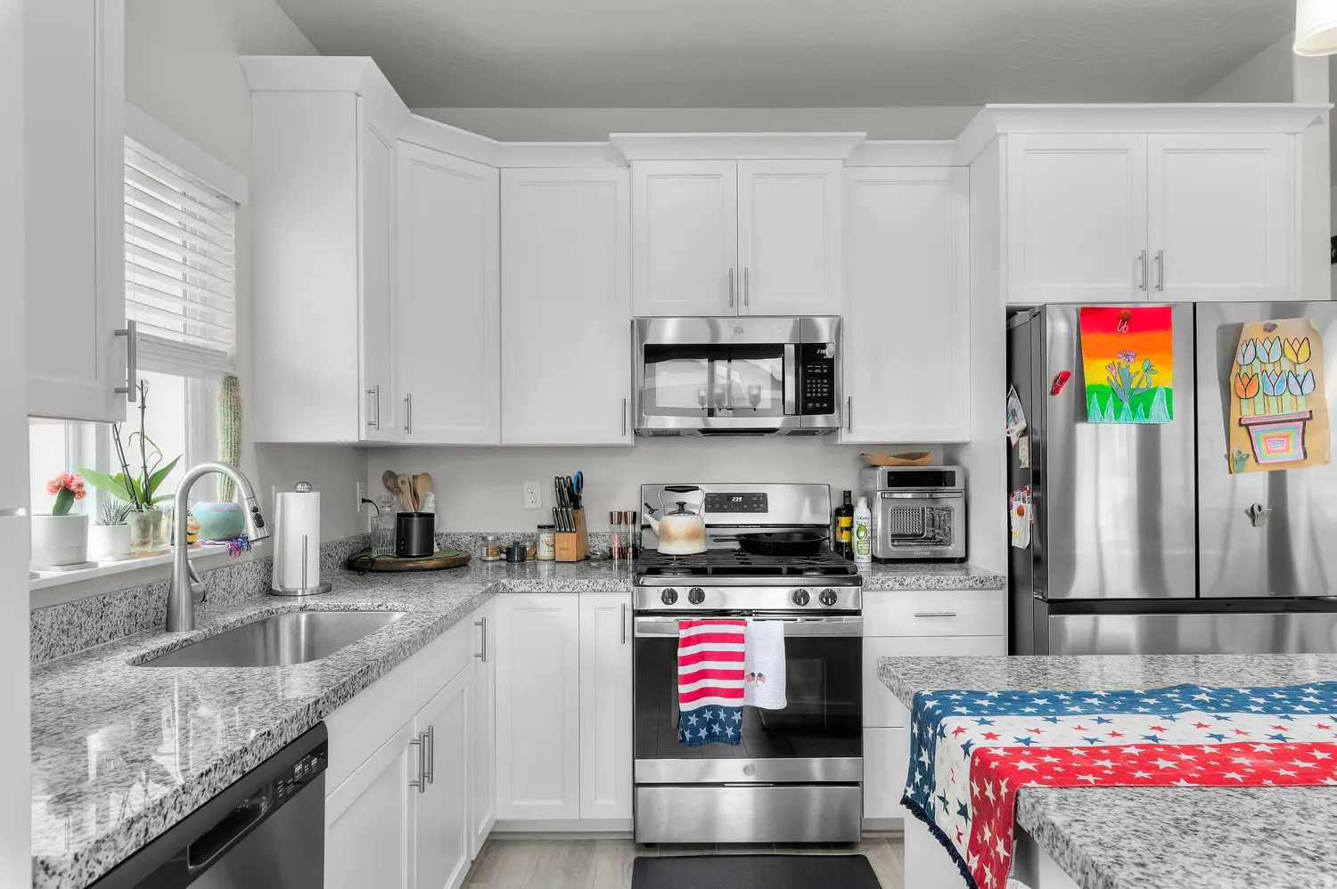 Kitchen featuring white shaker-style cabinetry, stainless steel appliances, speckled stone countertops, and a stainless steel sink with a gooseneck faucet
