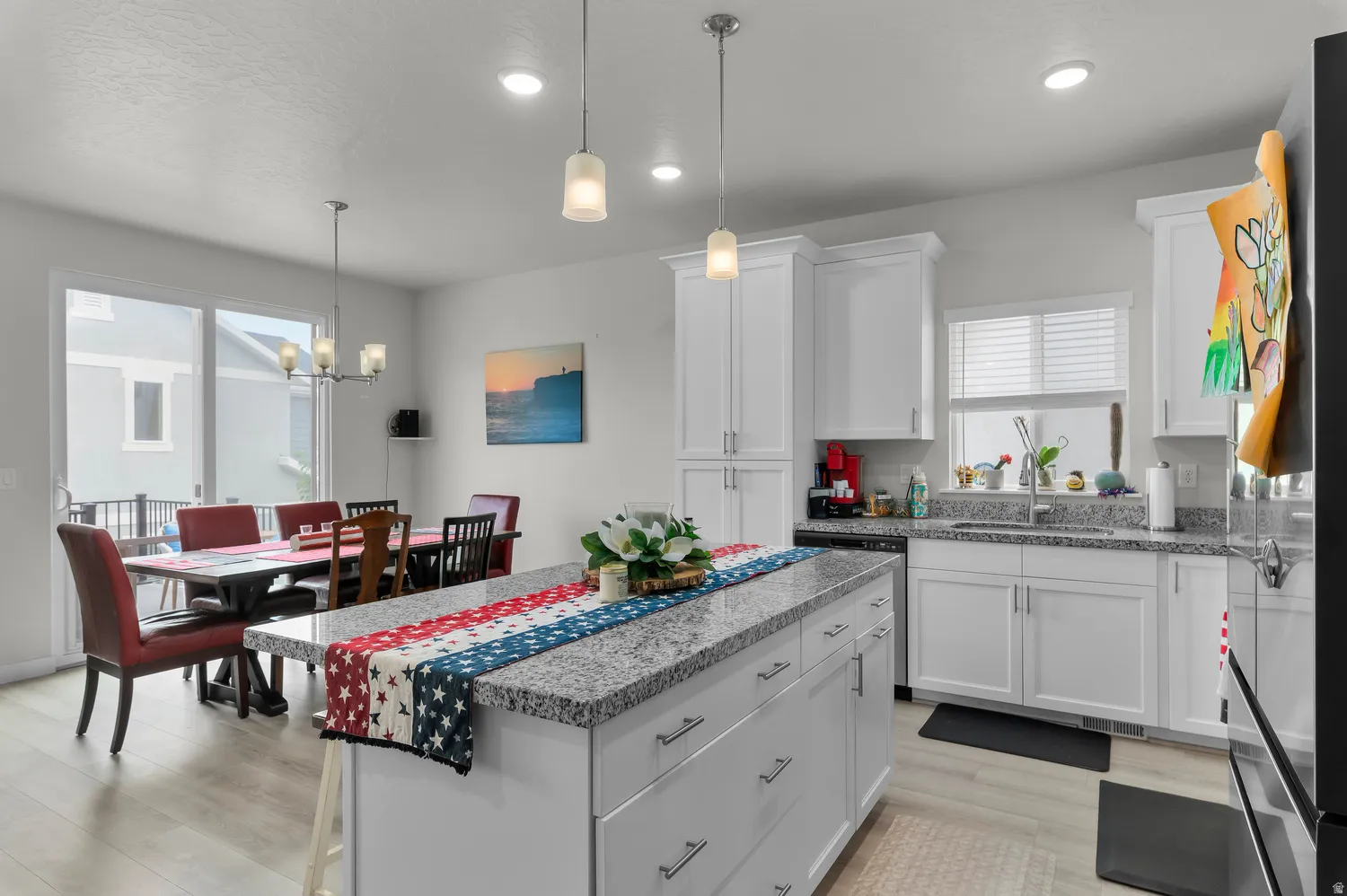 Open-concept kitchen and dining area featuring a central island with a granite countertop, white cabinetry, stainless steel appliances, and wood-finish flooring