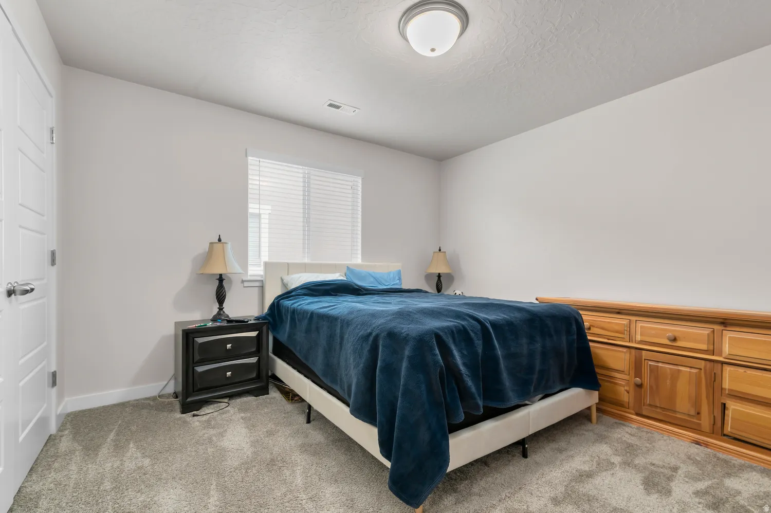 Carpeted room featuring a window with blinds, white paneled door, and a flush mount ceiling light fixture