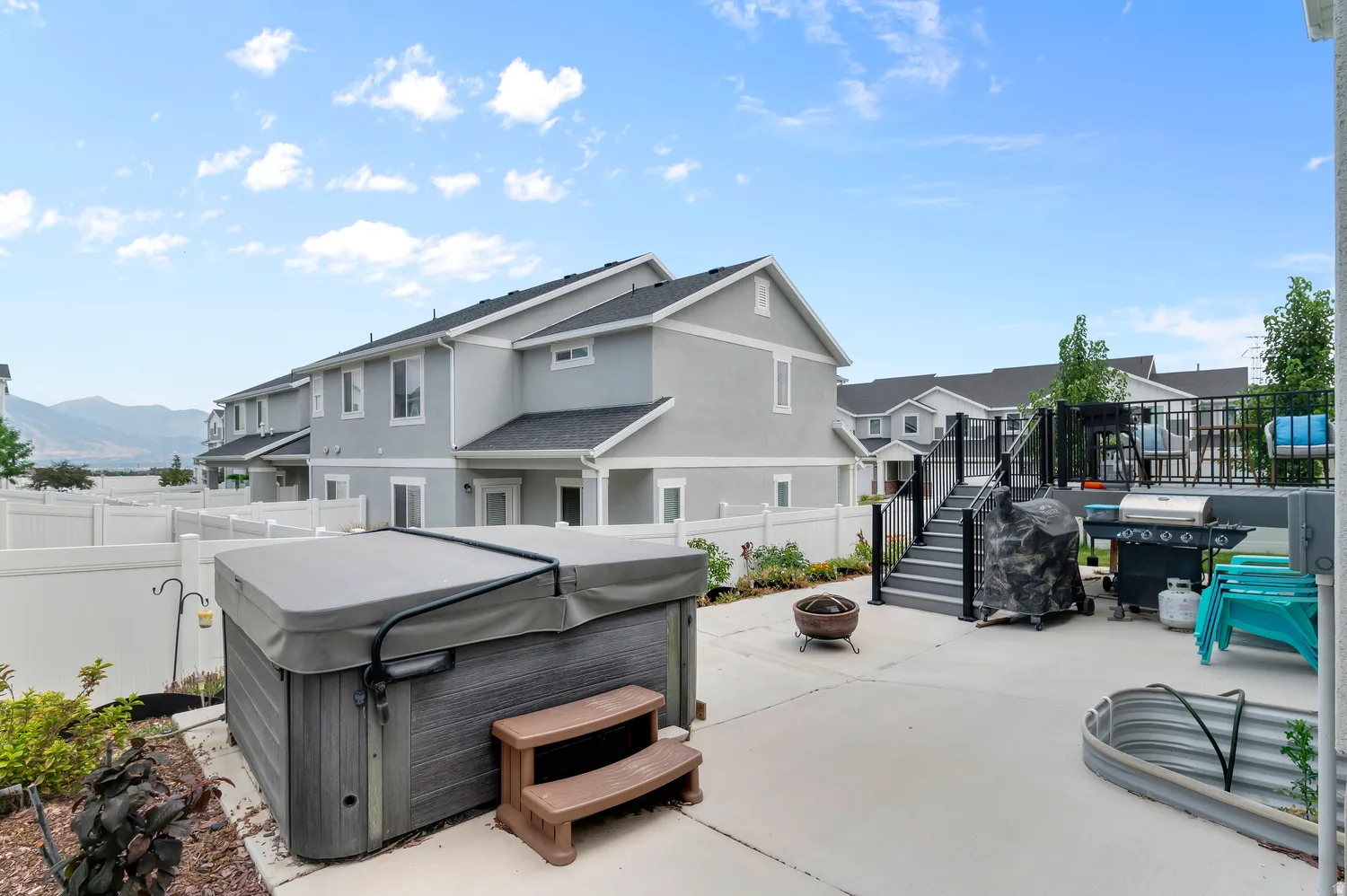 Patio area featuring a hot tub, concrete paving, a fire pit, and a tiered deck with black railings