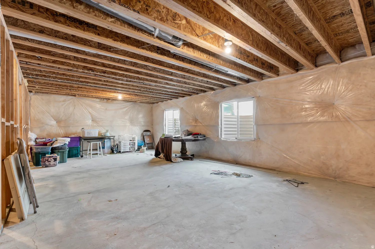 Unfinished basement offering exposed wood ceiling joists, concrete flooring, and multiple window openings