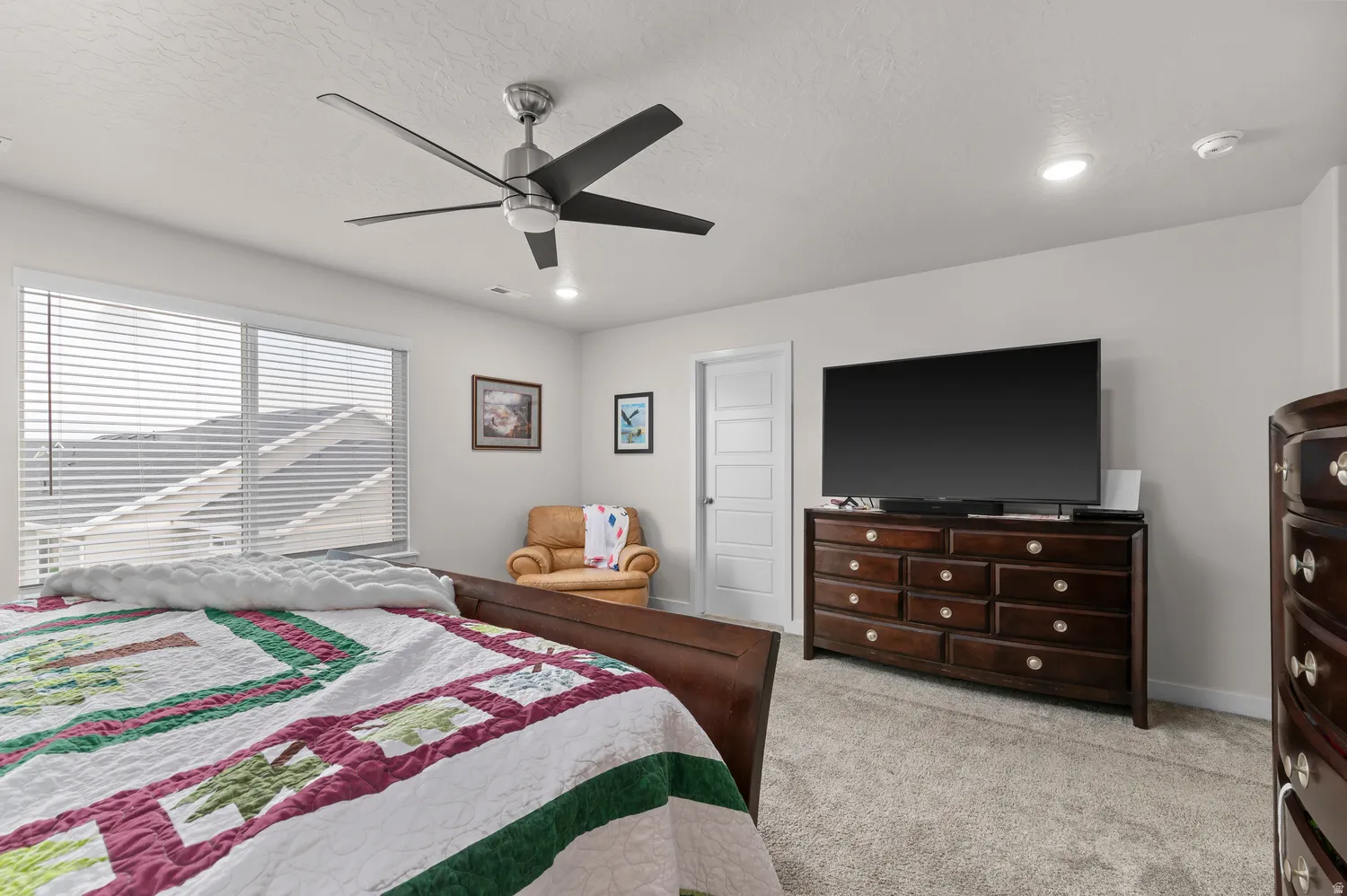 Carpeted bedroom with a dark wood-finish bed frame, large window with horizontal blinds, and a five-panel interior door