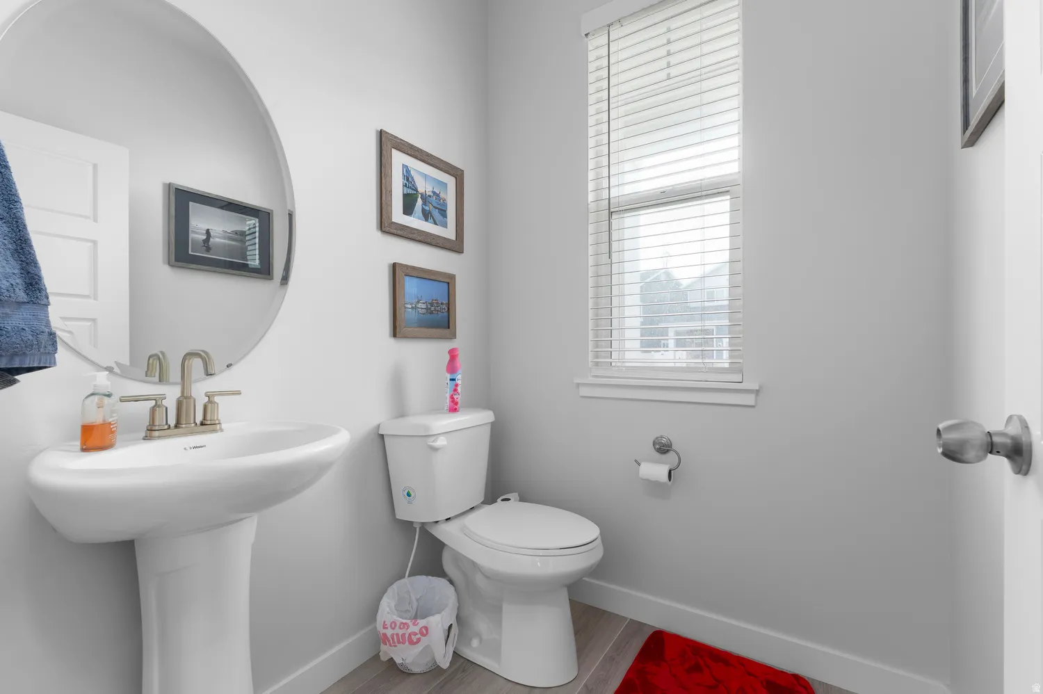 Pedestal sink with brushed nickel faucet, round wall-mounted mirror, and light gray wood-finish flooring