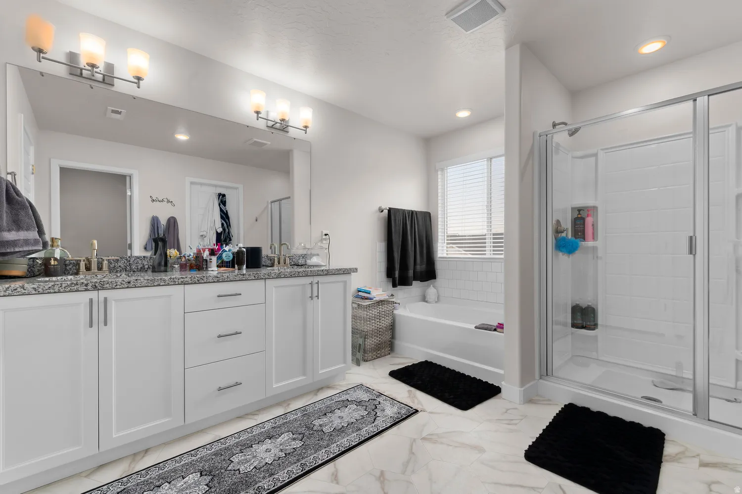 Spacious bathroom featuring a double vanity with stone countertops, a full-width mirror, and two contemporary light fixtures