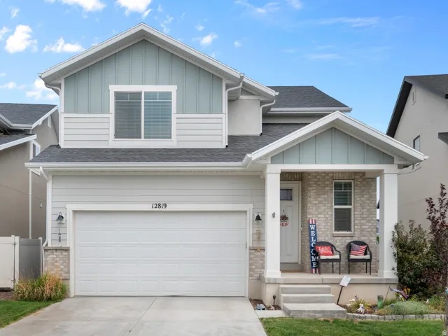 Contemporary two-story residence featuring a two-car garage, covered porch entry, and mixed material exterior with siding and stone accents