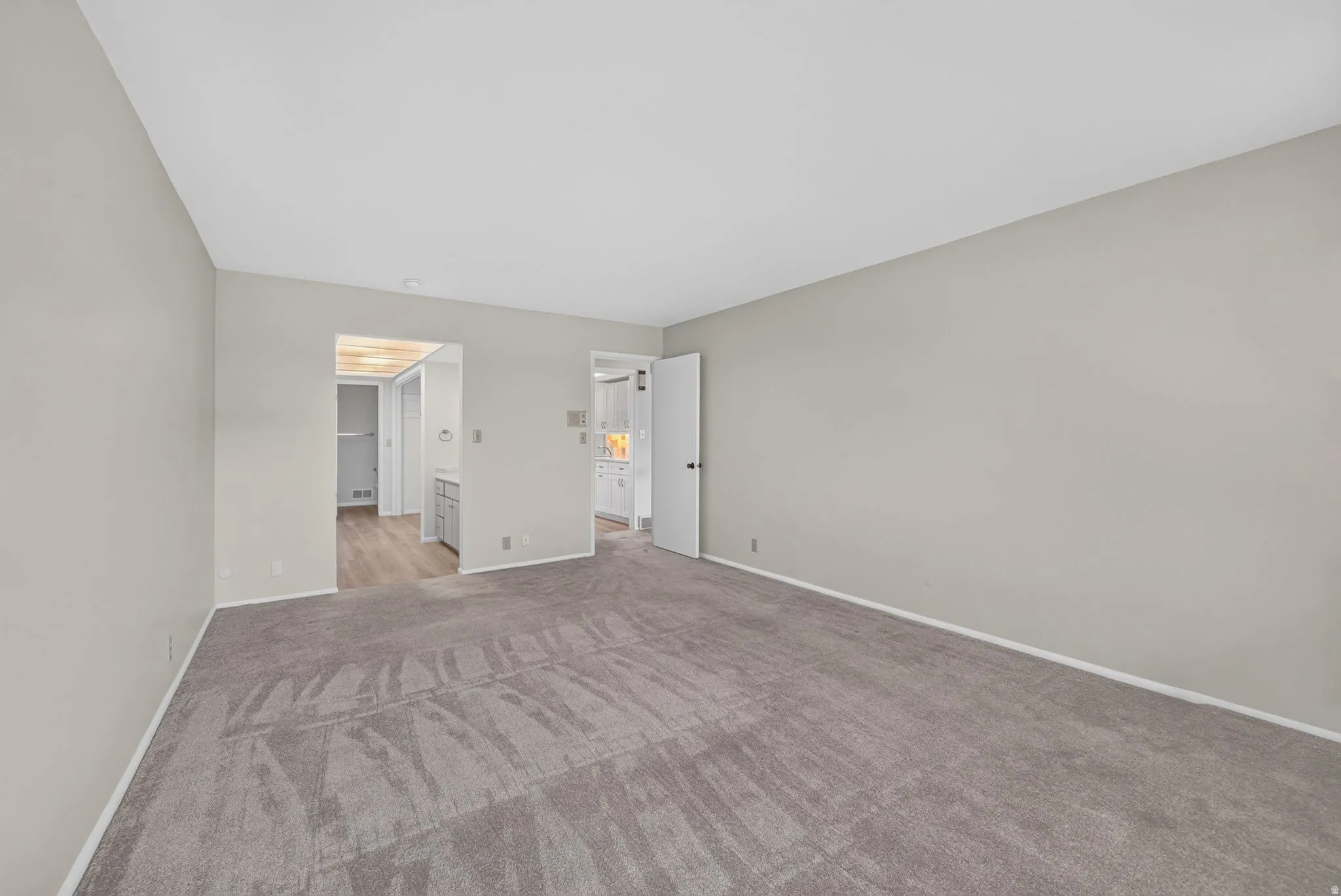 Spacious carpeted room featuring light gray walls, white baseboards, and two doorways with white trim