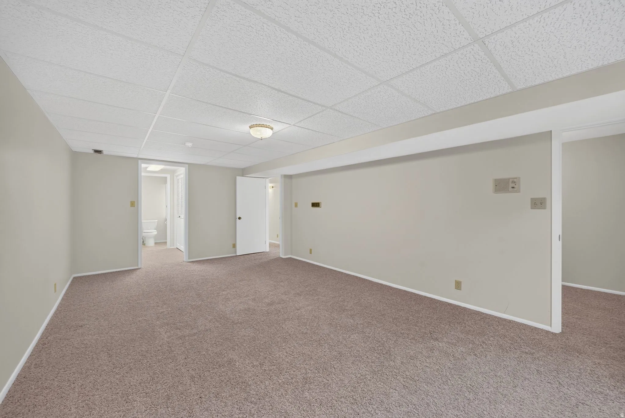 Spacious carpeted room featuring a drop-tile ceiling and recessed lighting