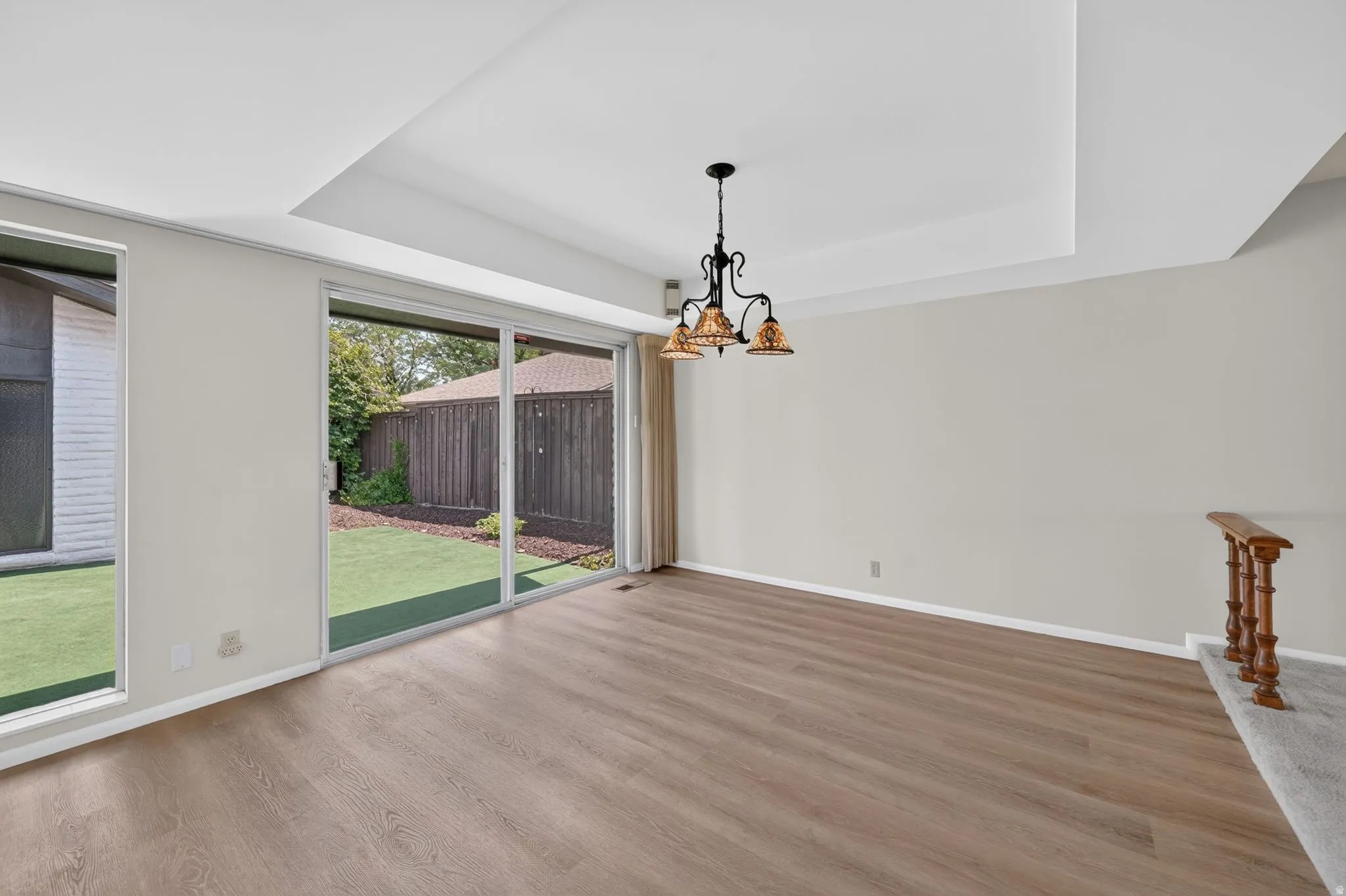 Spacious room featuring wood-finish flooring, a tray ceiling, and a decorative chandelier