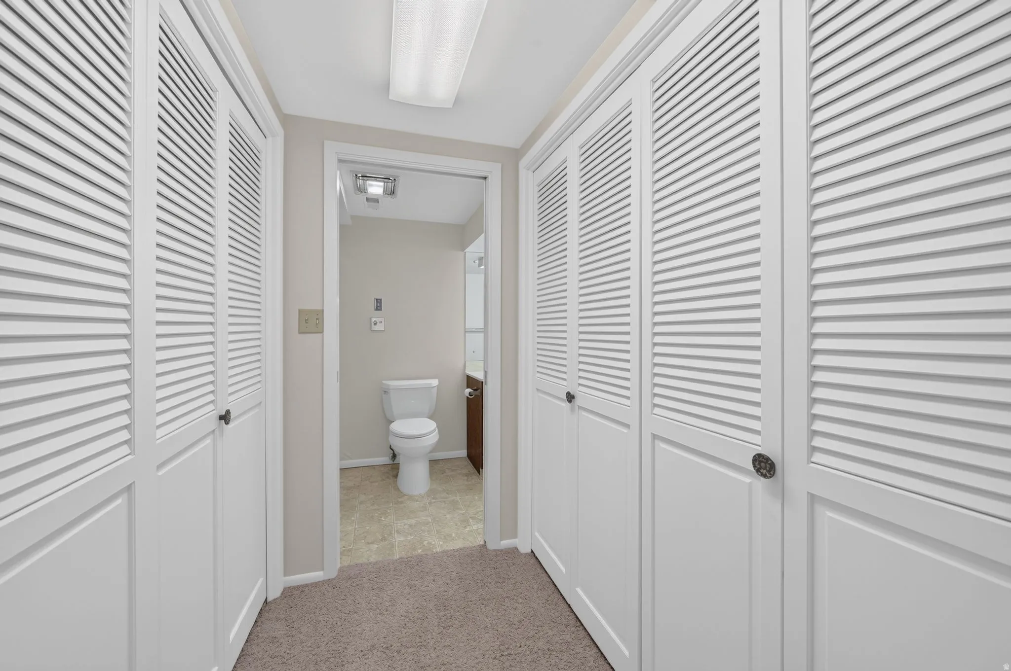 Hallway featuring multiple louvered bifold closet doors, recessed lighting, and carpet flooring