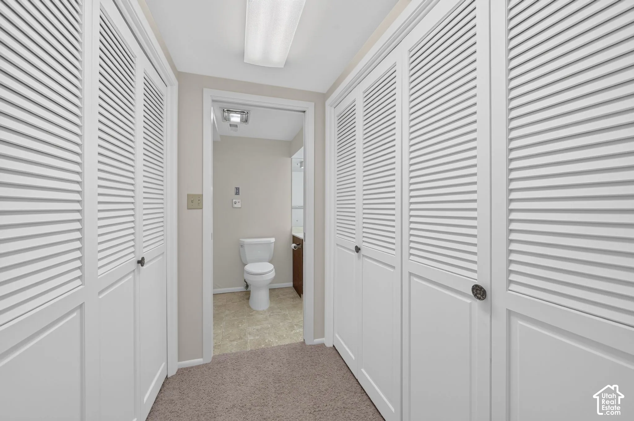 Hallway featuring multiple louvered bifold closet doors, recessed lighting, and carpet flooring