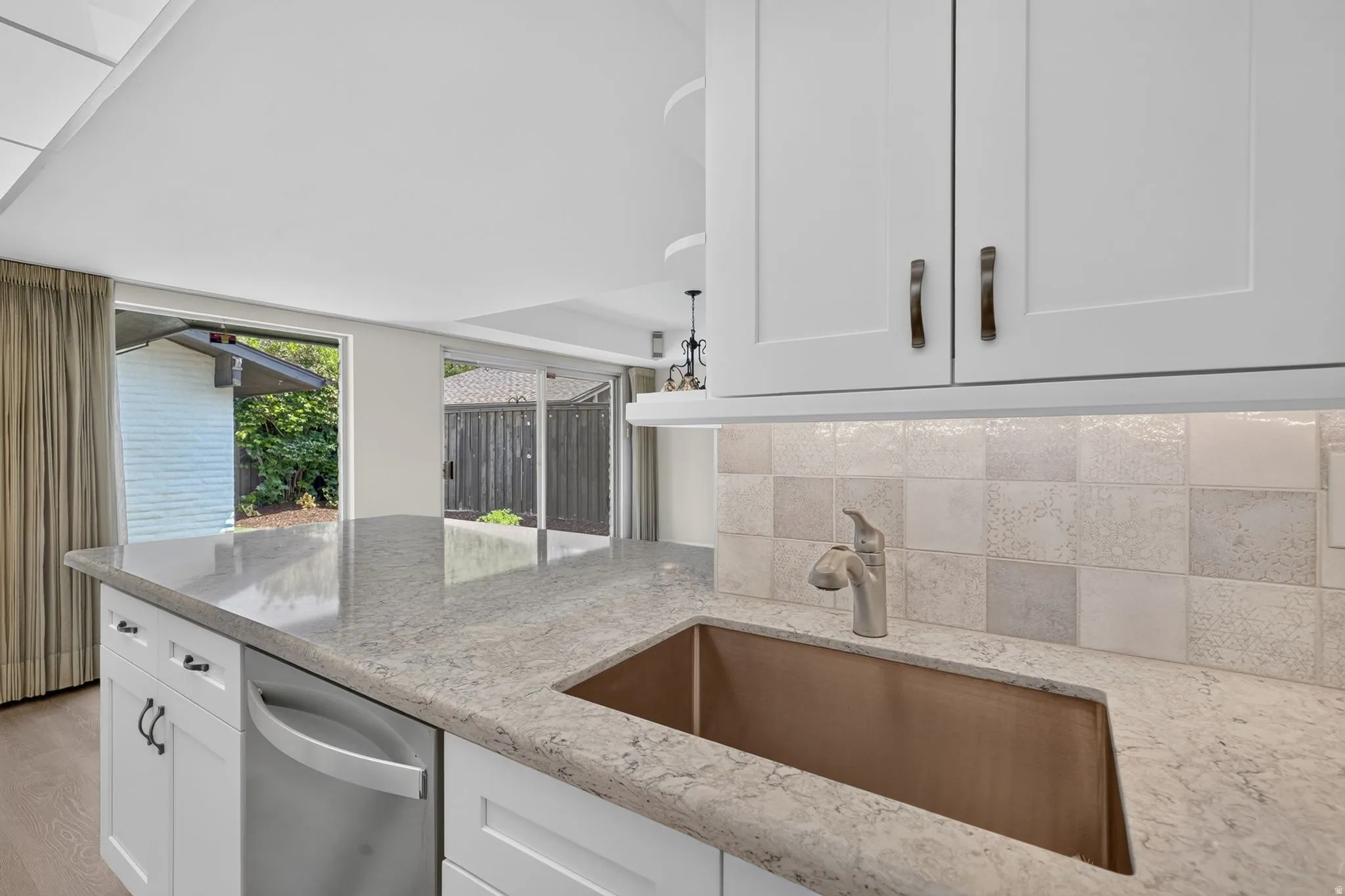 White cabinetry with bronze hardware, a stainless steel dishwasher, and a stone-finish countertop featuring an undermount copper sink