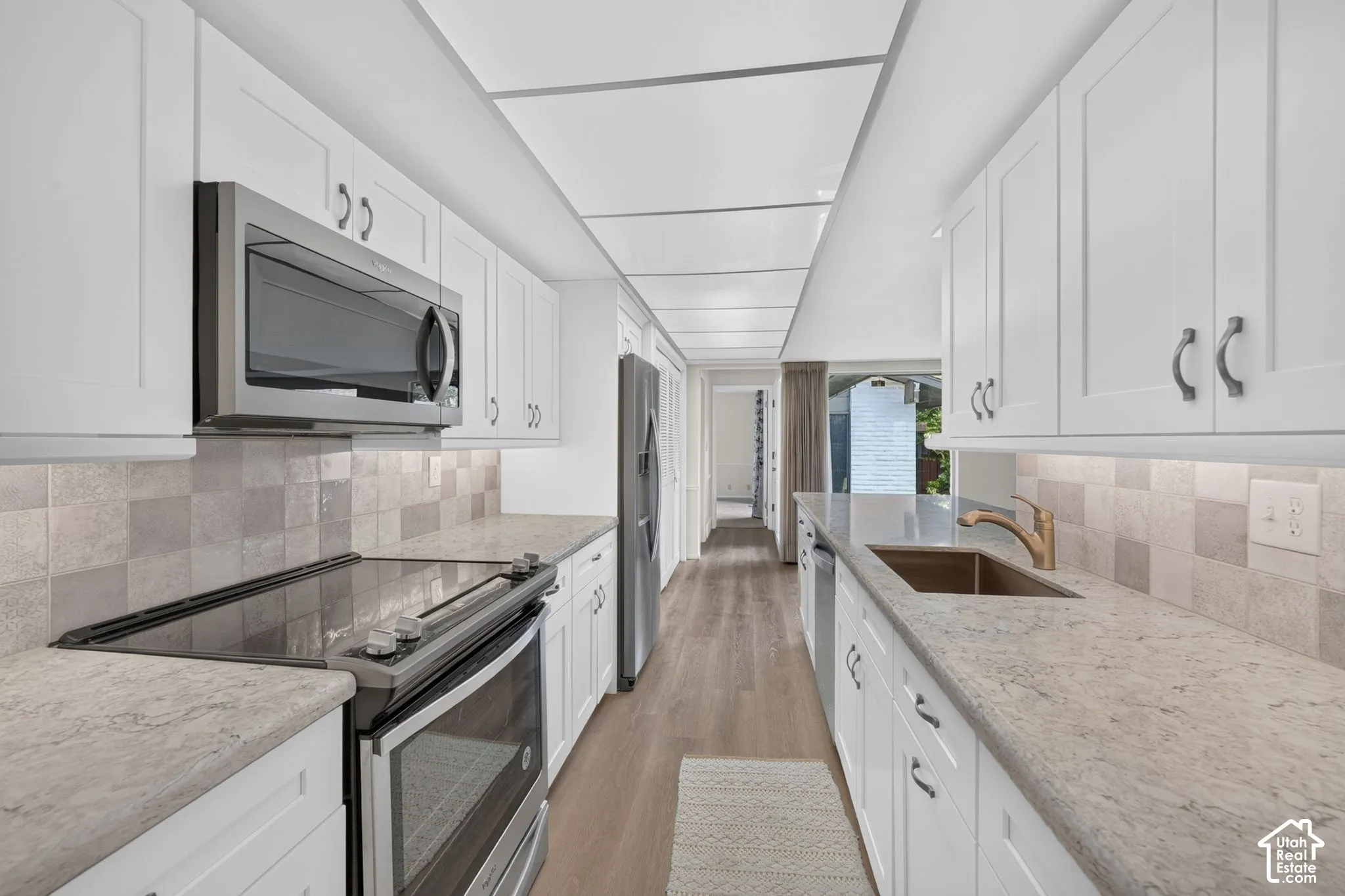 Galley kitchen featuring white shaker cabinetry, light-toned countertops, and wood-finish flooring