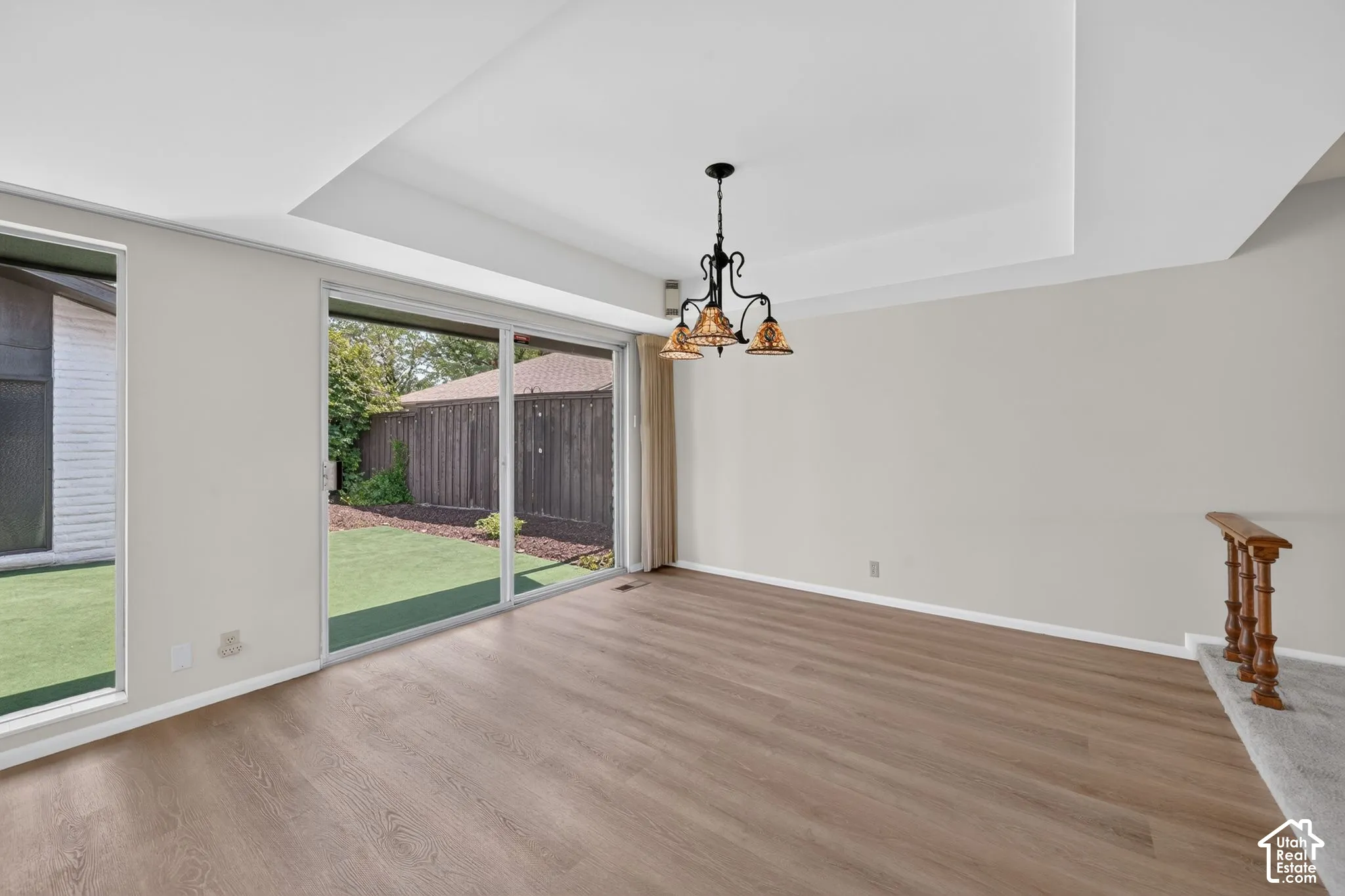 Spacious room featuring wood-finish flooring, a tray ceiling, and a decorative chandelier