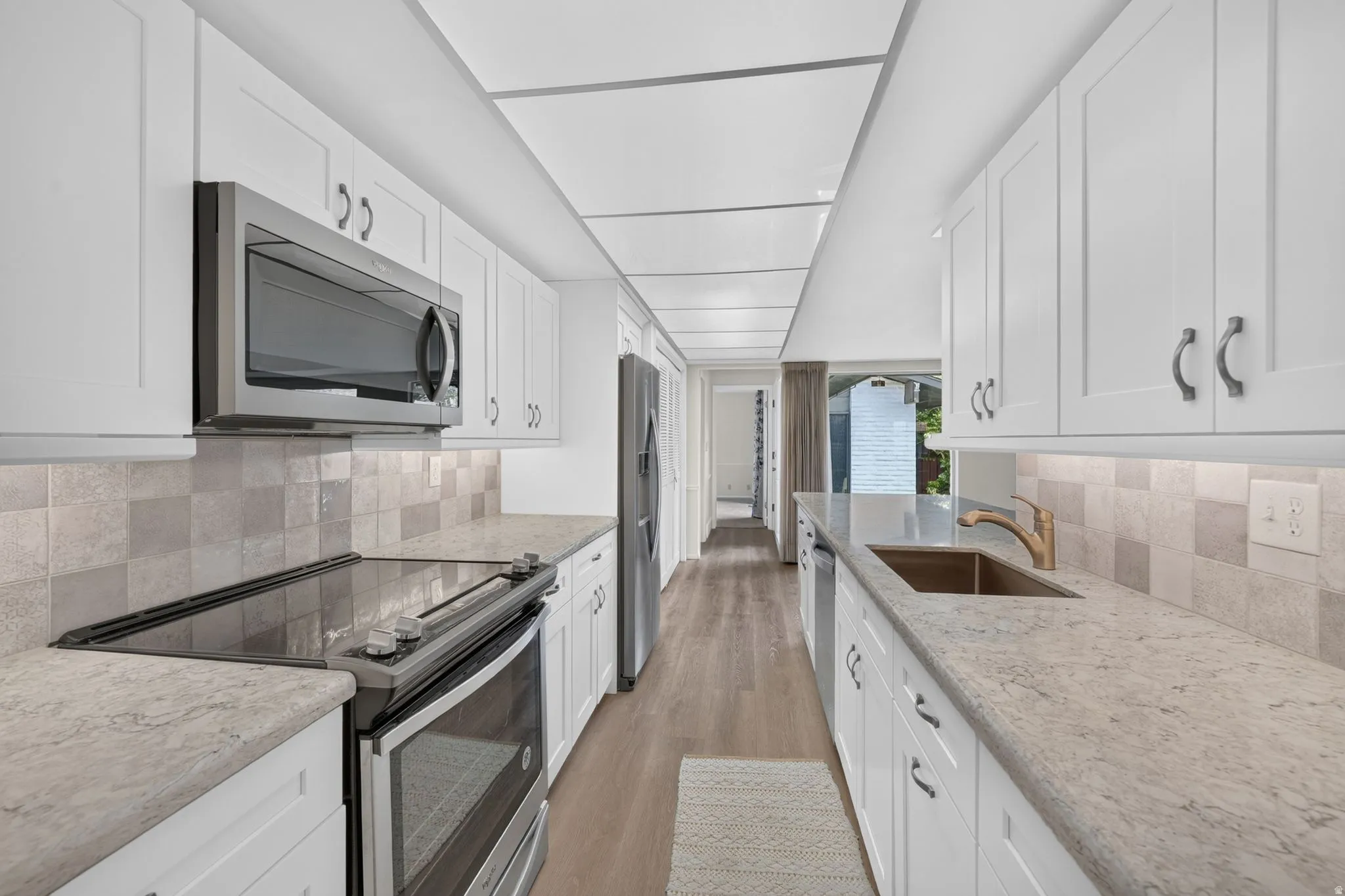 Galley kitchen featuring white shaker cabinetry, light-toned countertops, and wood-finish flooring