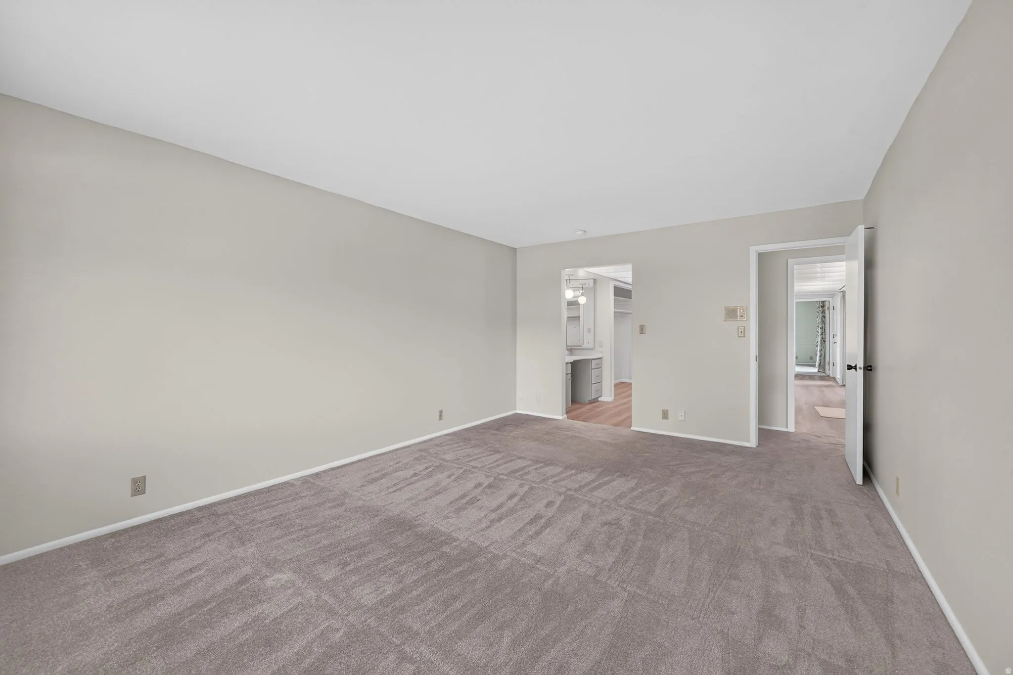 Spacious room featuring neutral carpeting, light-toned walls, and white trim