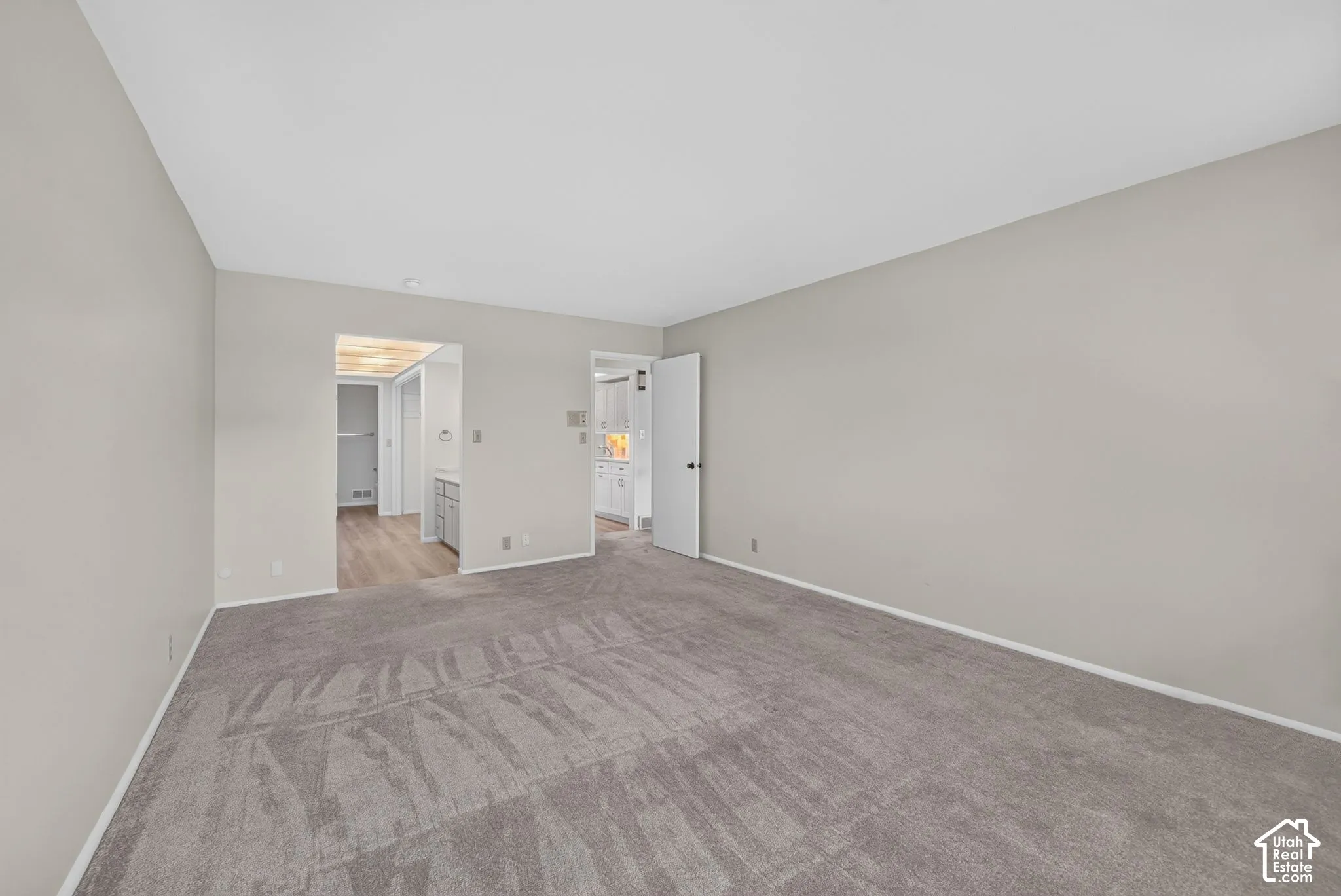 Spacious carpeted room featuring light gray walls, white baseboards, and two doorways with white trim