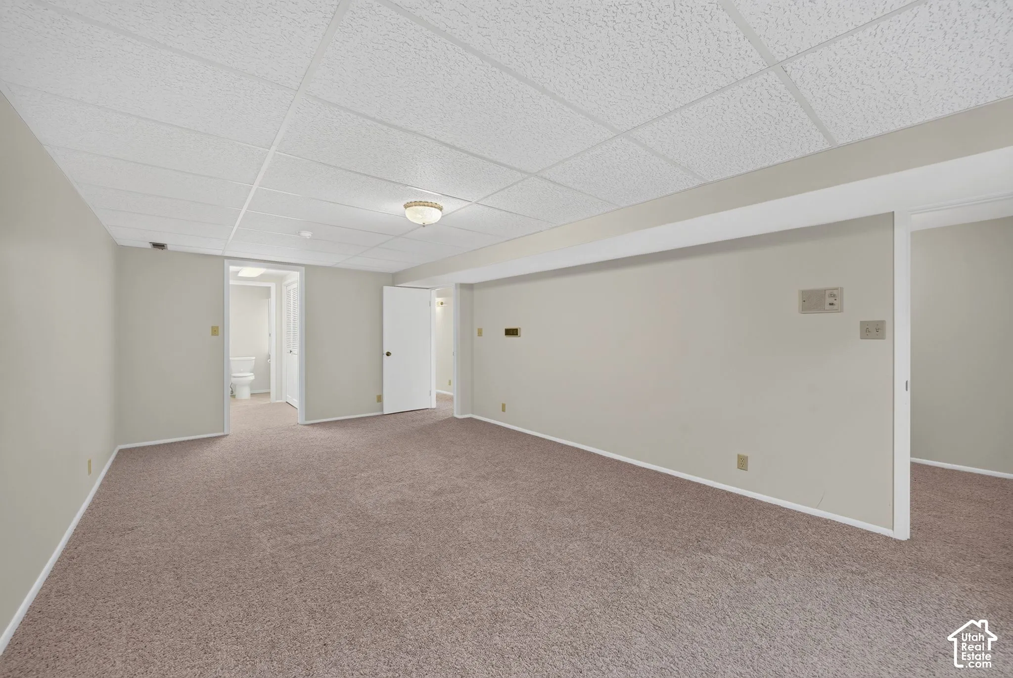 Spacious carpeted room featuring a drop-tile ceiling and recessed lighting
