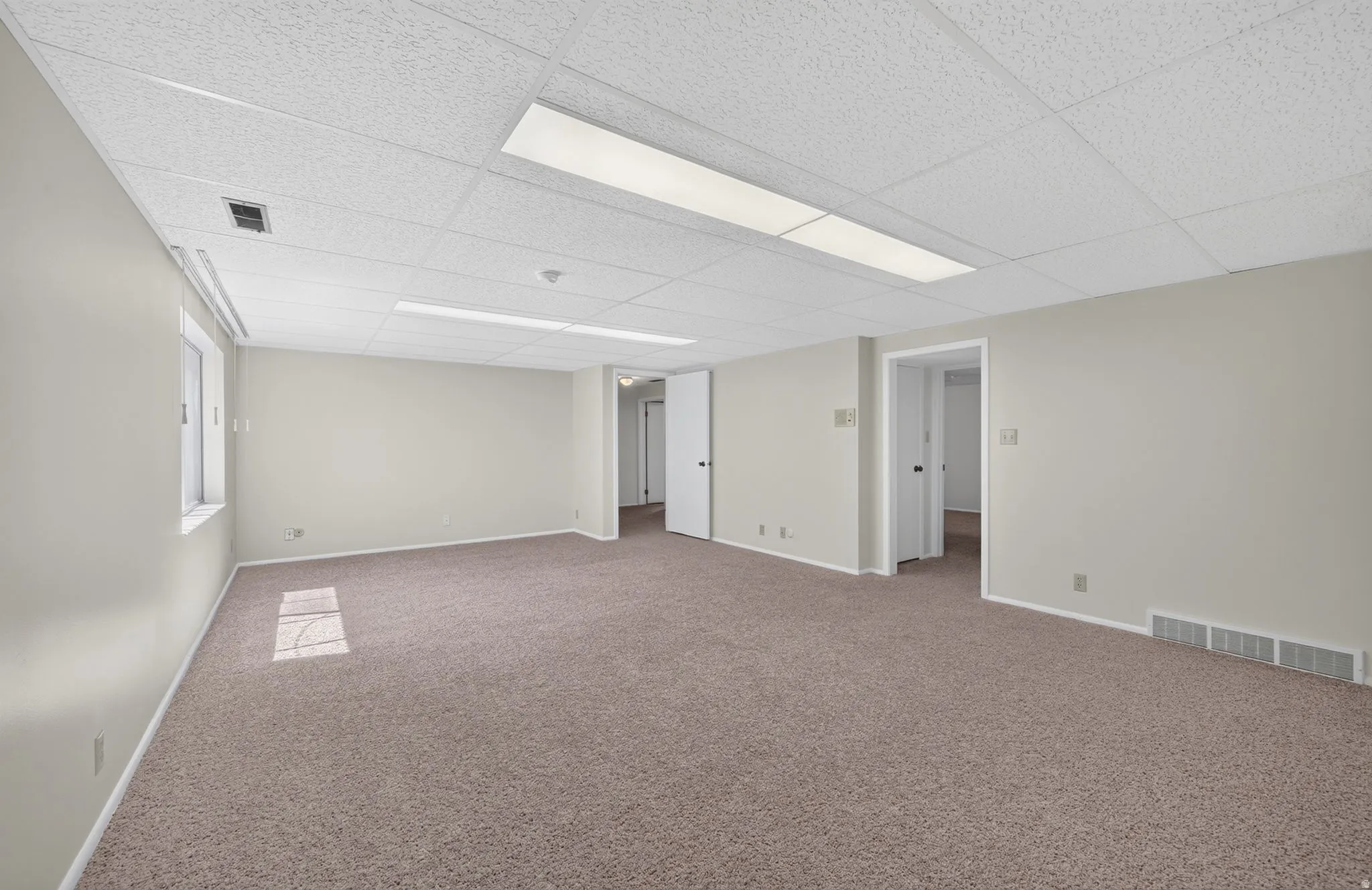 Spacious room featuring neutral carpeting, light-toned walls, and a drop ceiling with recessed lighting