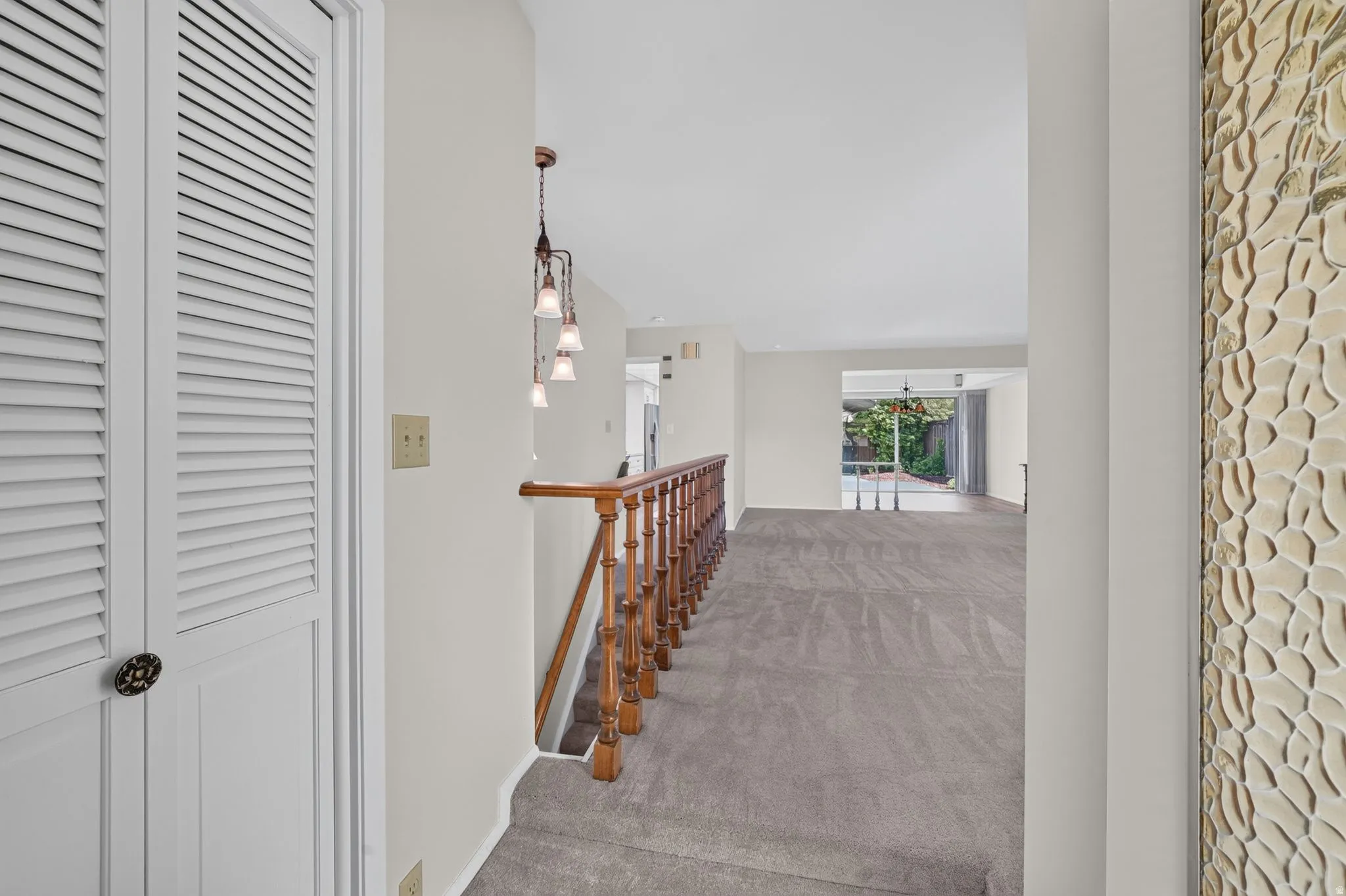 Upper-level landing featuring wood banister, contemporary chandelier, and grey carpet flooring
