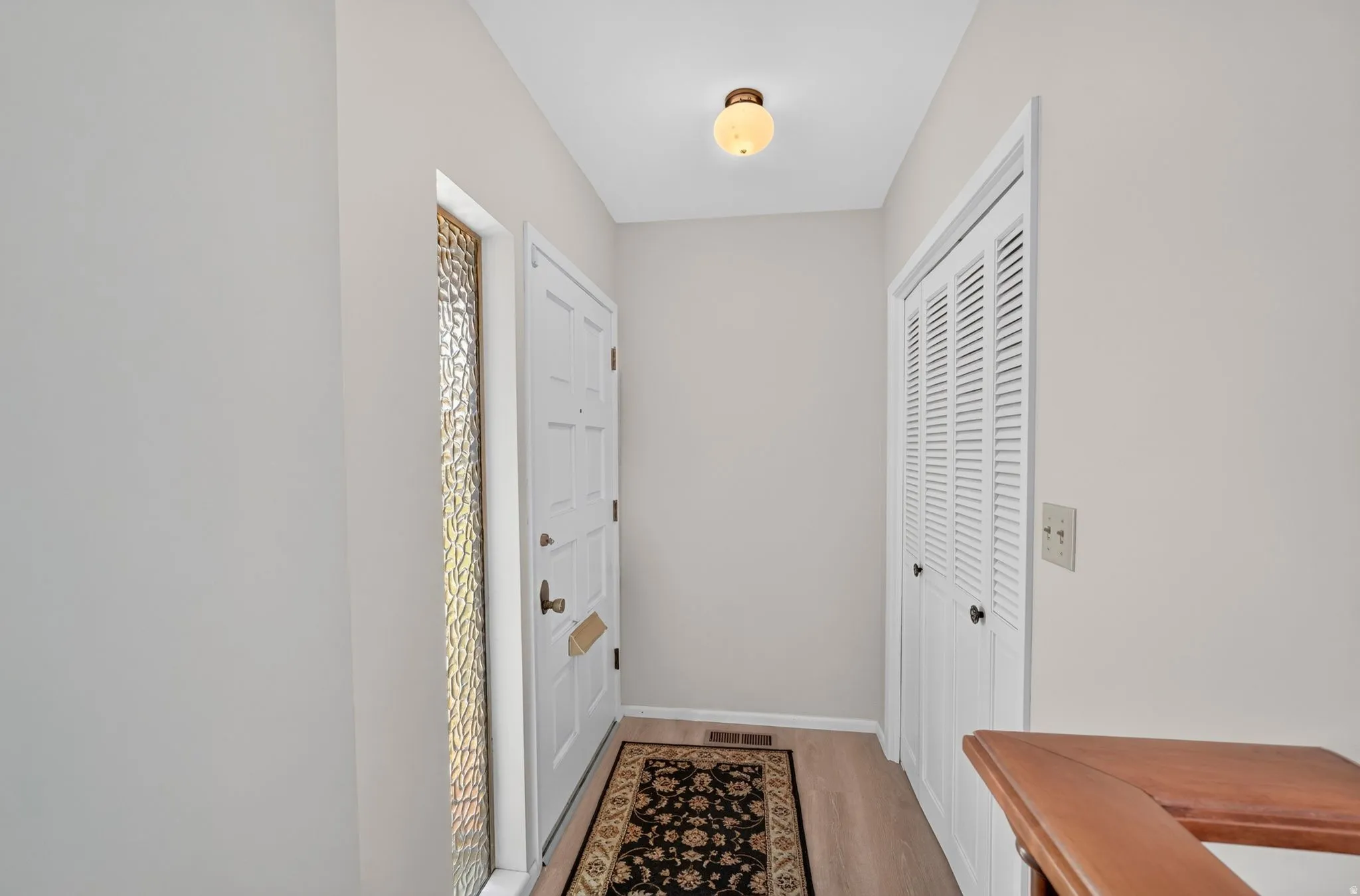 Entryway featuring a white paneled door with decorative sidelight, wood-finish flooring, bi-fold louvered closet doors, and a ceiling-mounted fixture