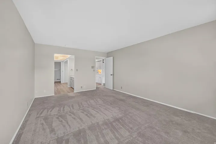 Spacious carpeted room featuring light gray walls, white baseboards, and two doorways with white trim