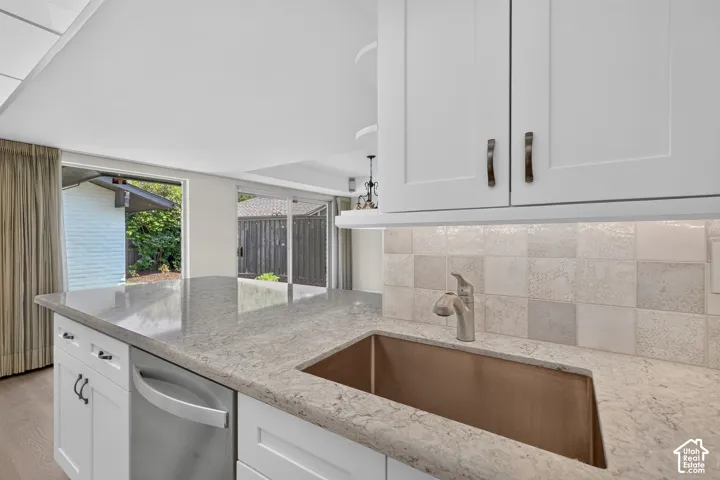 White cabinetry with bronze hardware, a stainless steel dishwasher, and a stone-finish countertop featuring an undermount copper sink