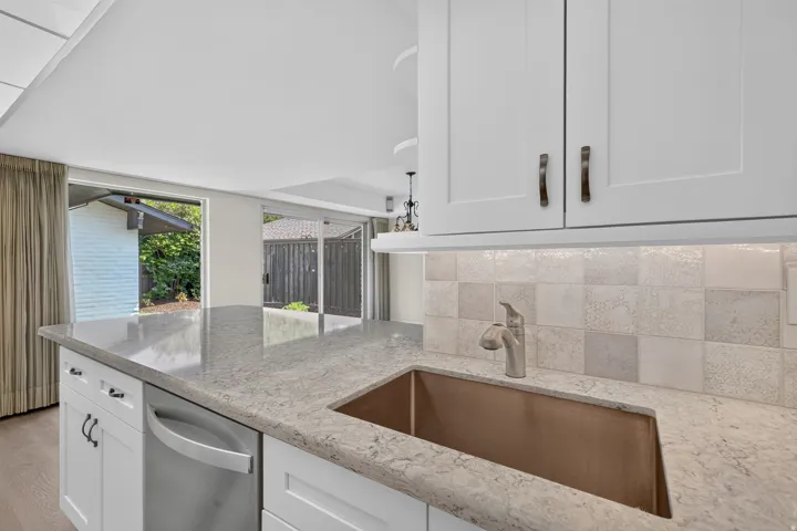 White cabinetry with bronze hardware, a stainless steel dishwasher, and a stone-finish countertop featuring an undermount copper sink