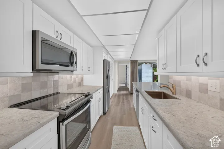 Galley kitchen featuring white shaker cabinetry, light-toned countertops, and wood-finish flooring