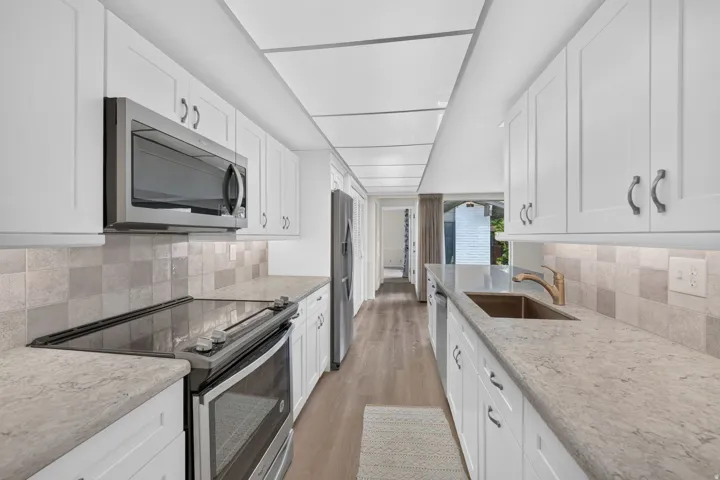 Galley kitchen featuring white shaker cabinetry, light-toned countertops, and wood-finish flooring