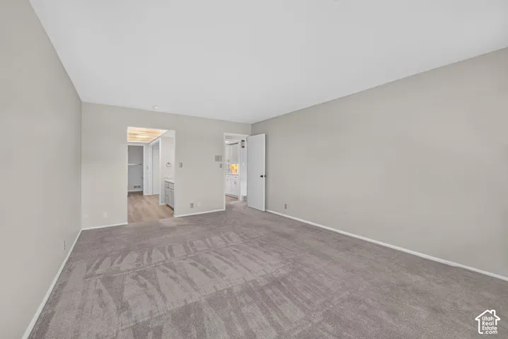 Spacious carpeted room featuring light gray walls, white baseboards, and two doorways with white trim