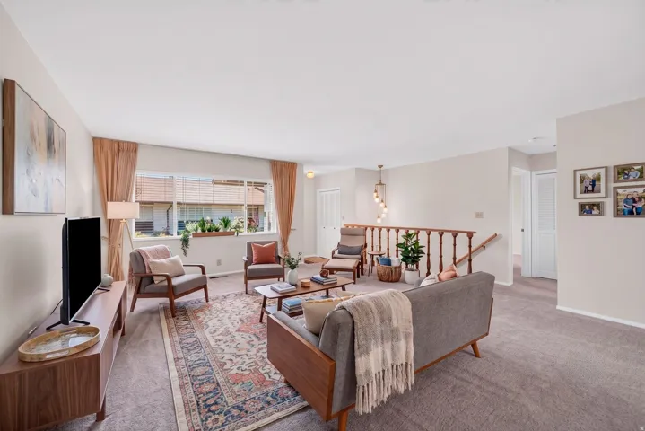 Spacious living area featuring neutral carpeting, a large picture window, and a wood railing staircase