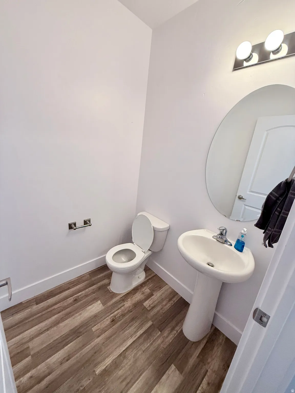 Half bath on the 2nd level at the top of the stairs coming up from the Entry/Foyer: featuring wood-finish flooring, a white pedestal sink, a toilet, a circular mirror.