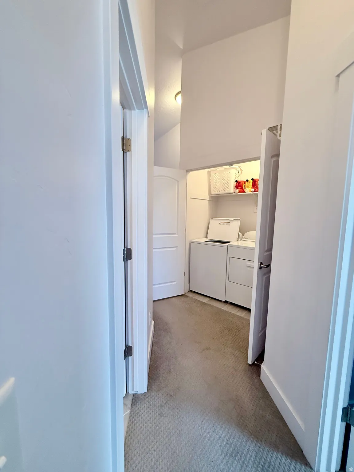 Dedicated laundry area featuring a washer and dryer, built-in shelving, and a light-colored carpeted hallway