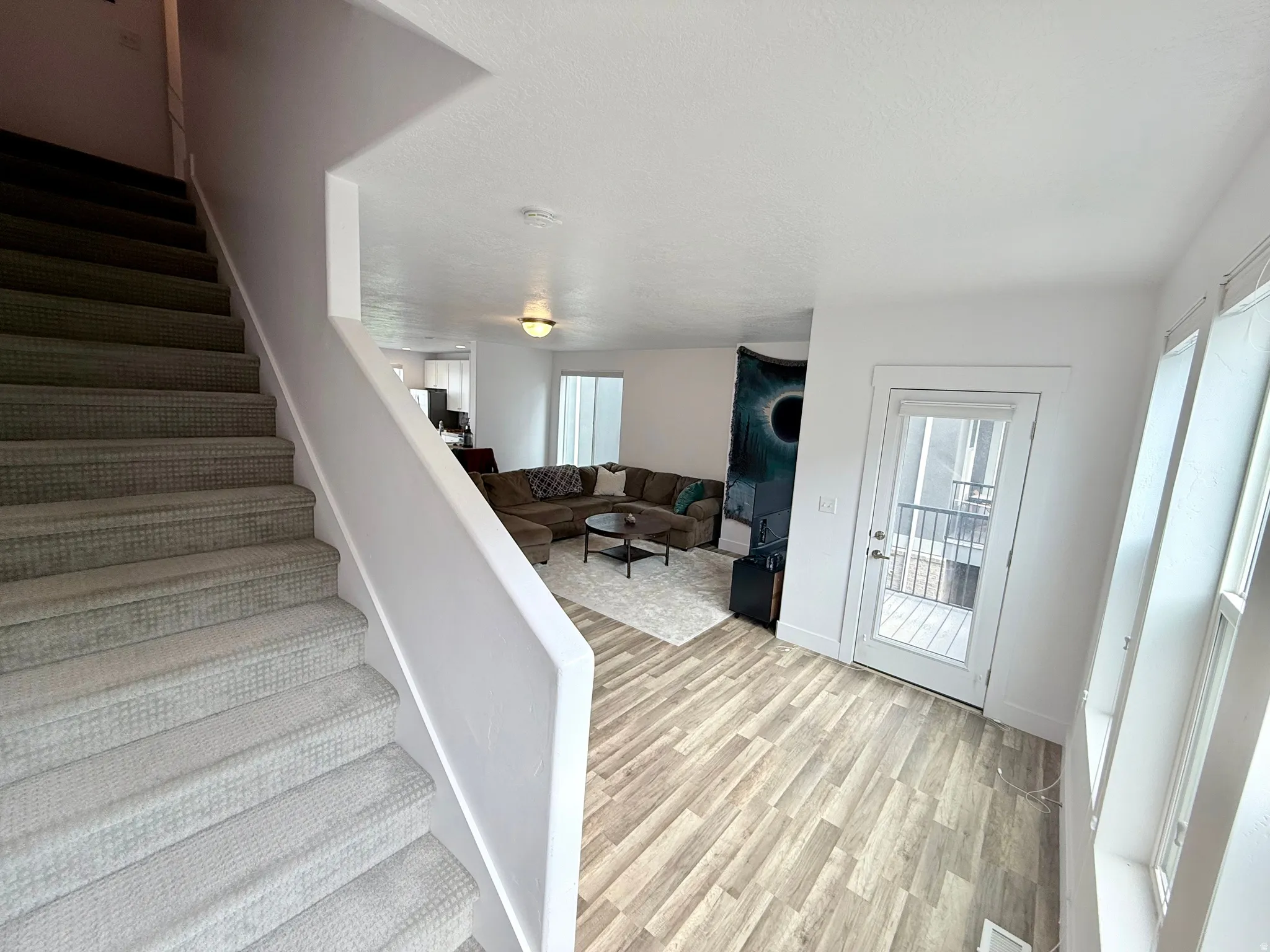Carpeted staircase leading up to the 3rd level/bedrooms with white painted walls, wood-finish flooring, and a glass-paneled exterior door leading to the balcony/deck.