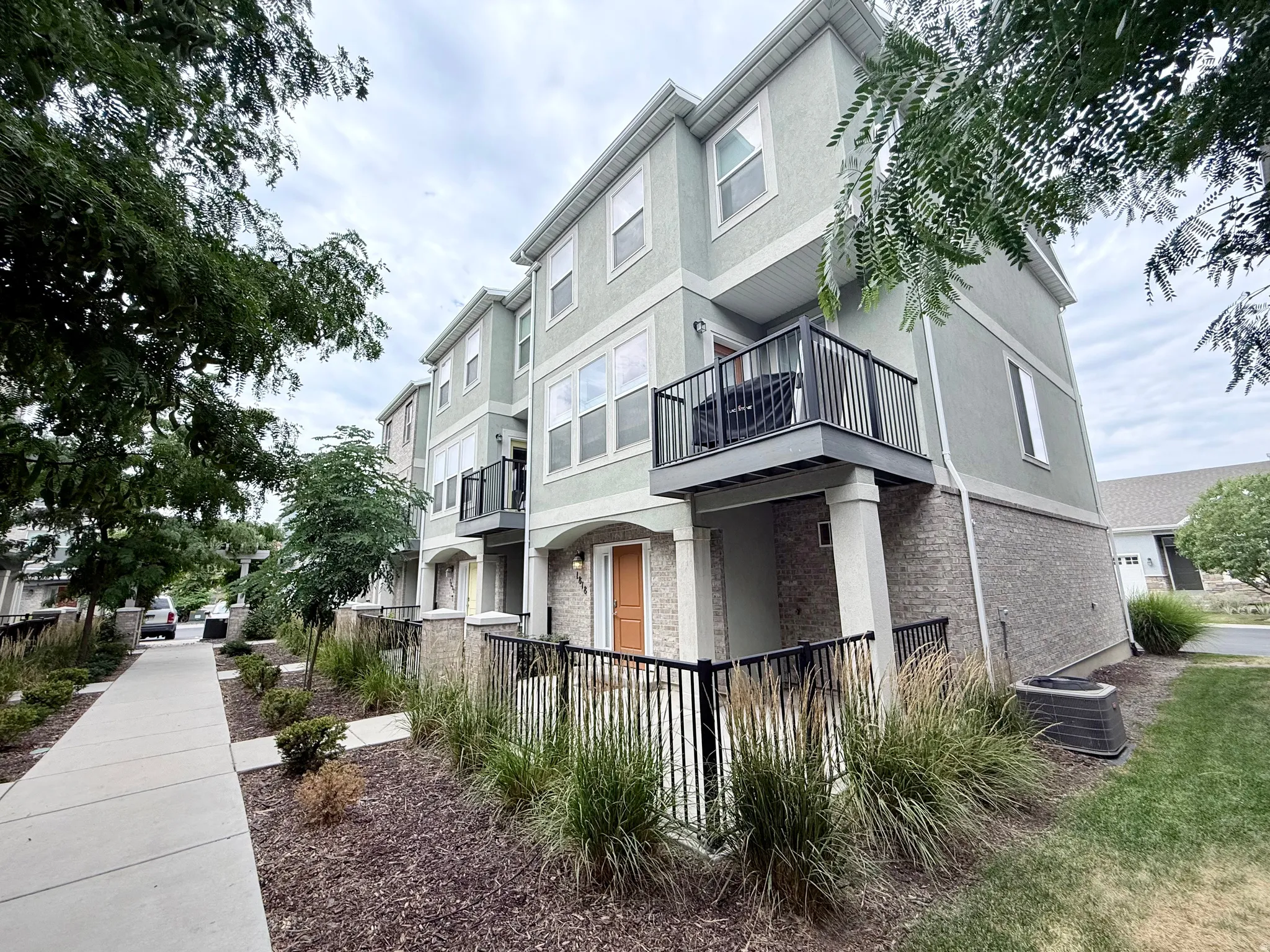 Contemporary townhome exterior featuring light green stucco and brick veneer siding