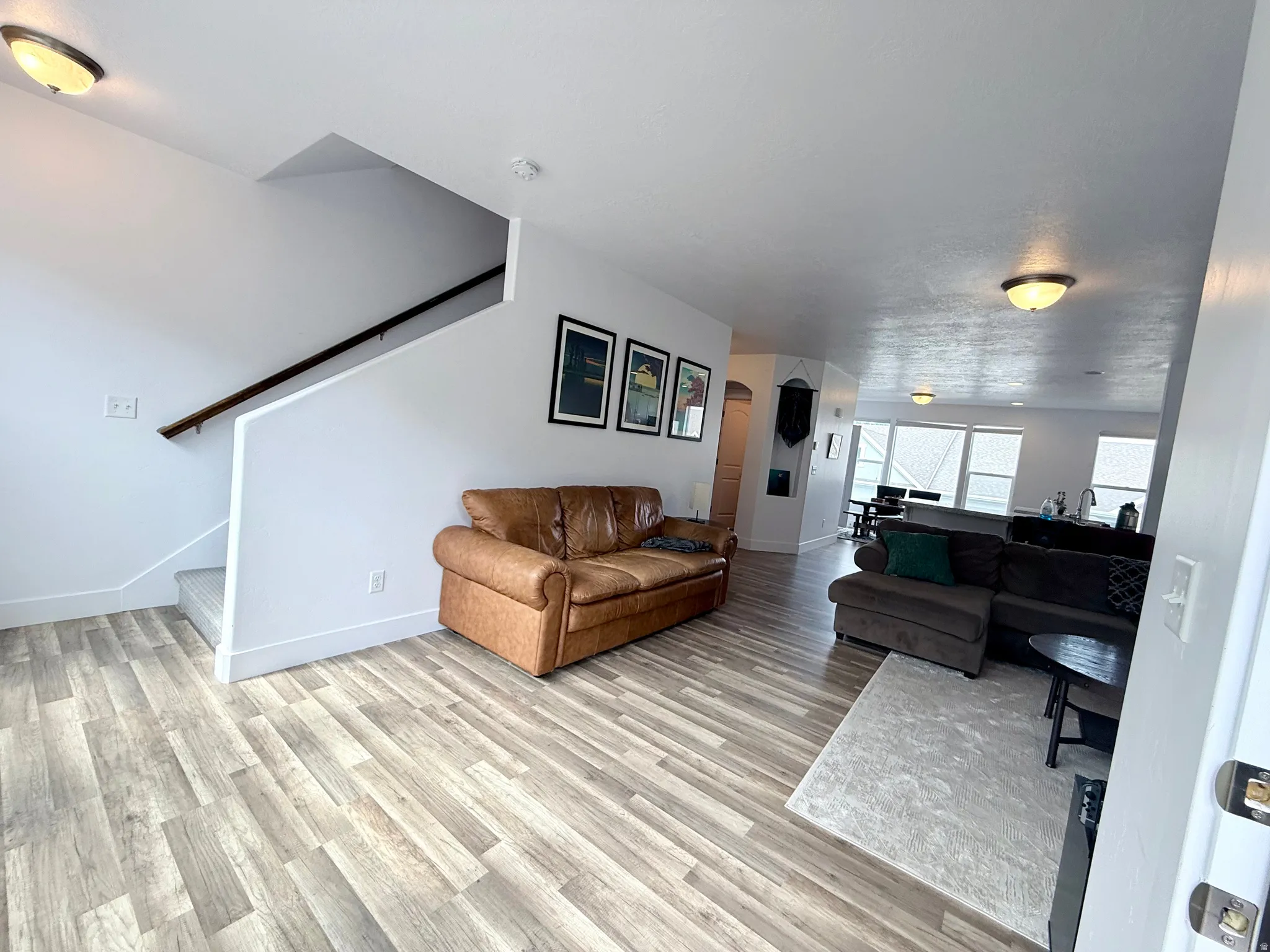 Open-concept living area with wood-finish flooring, a contemporary staircase with a dark wood handrail, and white baseboards