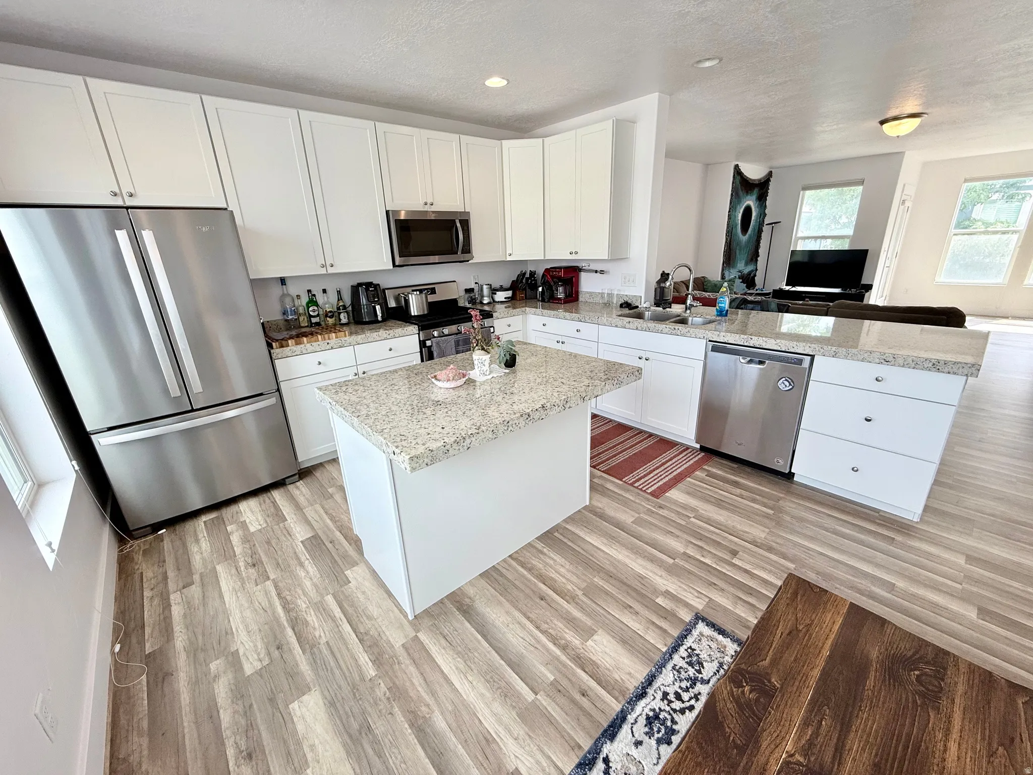 Open-concept kitchen featuring wood-finish flooring, white cabinetry, granite countertops, and stainless steel appliances including a refrigerator, microwave, and dishwasher