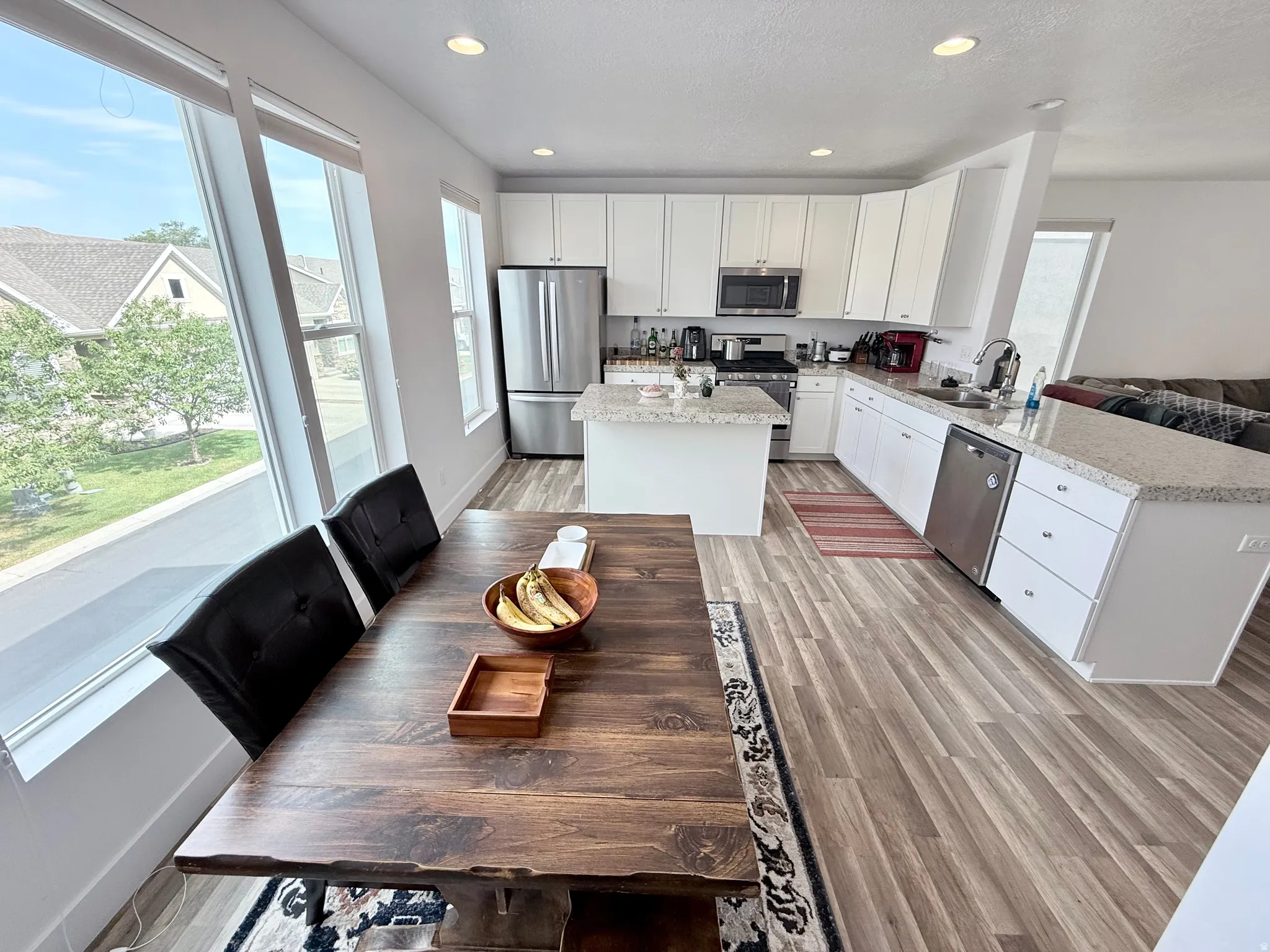 Open-concept kitchen featuring white cabinetry, stone countertops, stainless steel appliances, wood-finish flooring, and recessed lighting