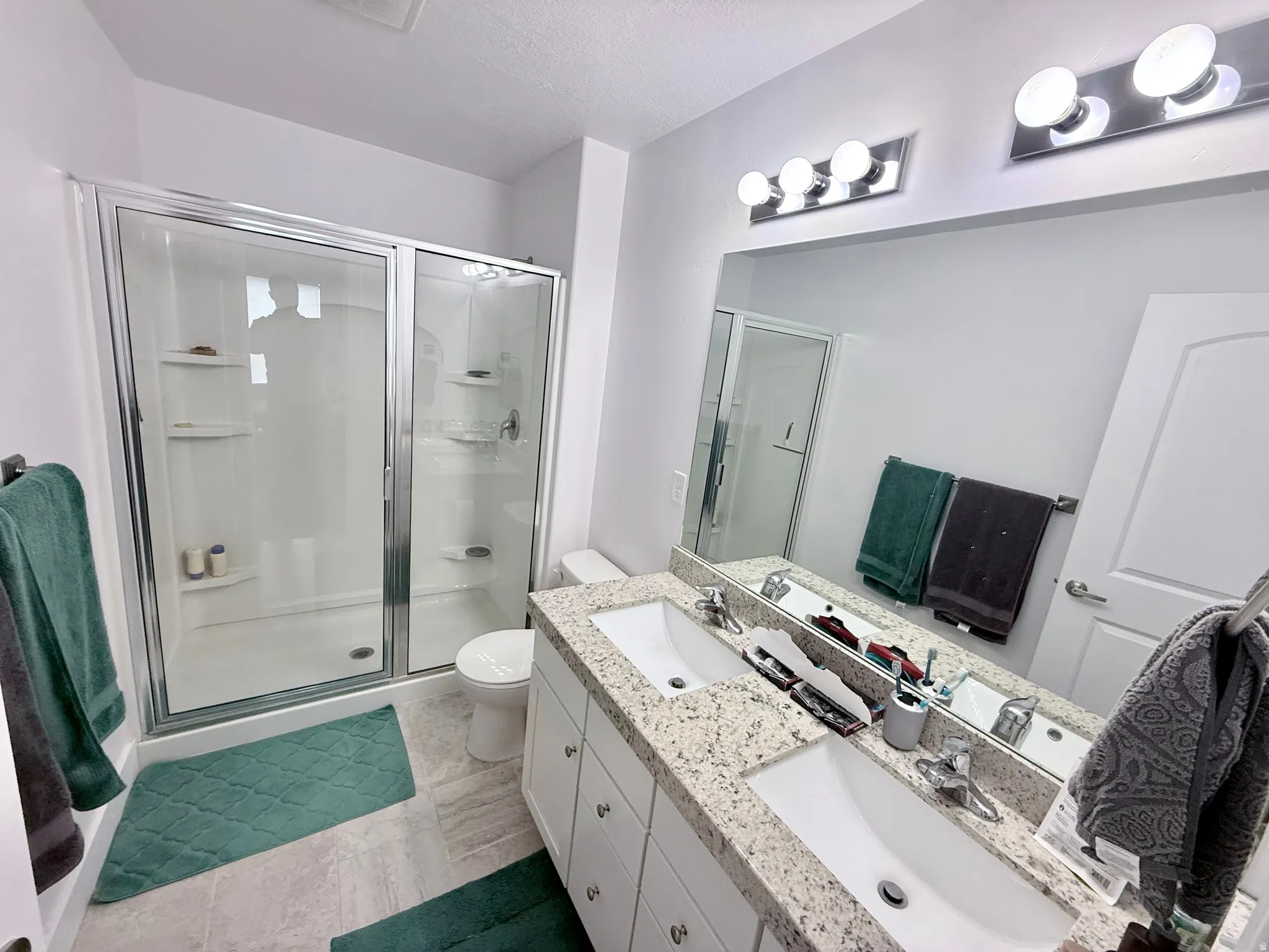 Spacious master bathroom featuring a dual vanity with a granite countertop, white cabinetry, and brushed nickel hardware