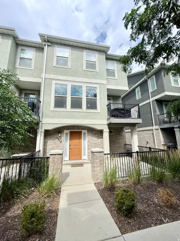 Three-story townhome with a light green stucco and brick facade