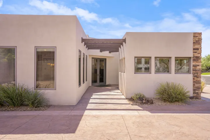 Contemporary facade featuring a stucco exterior, stone accent column, wood pergola, and stamped concrete walkway