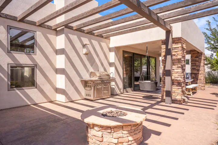 Expansive outdoor patio featuring a wood pergola, built-in stone fire pit, and a covered grilling area