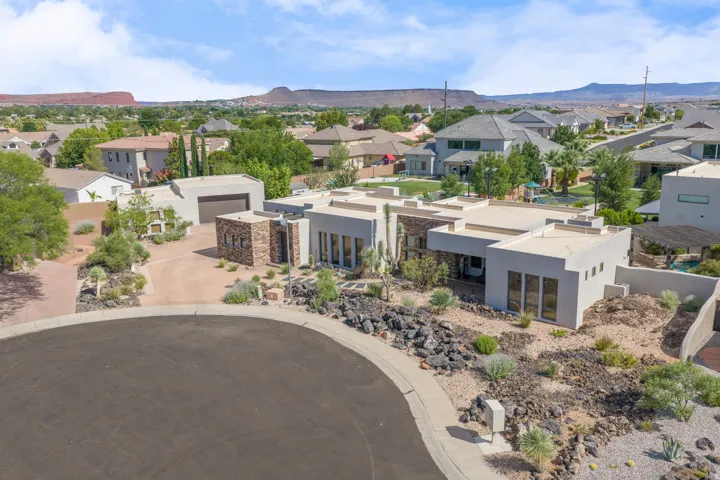 Modern desert-inspired residence featuring a flat roofline, stucco exterior, stacked stone accents, a multi-car garage, and desert landscaping