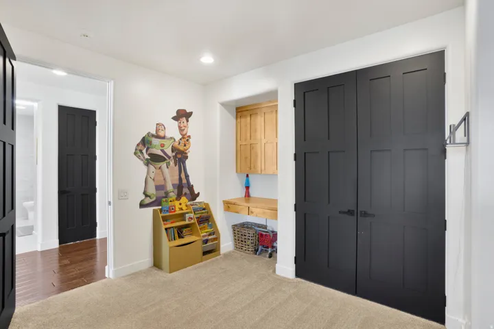 Light beige carpeting complemented by white walls, black paneled doors, a built-in wooden desk, and recessed lighting