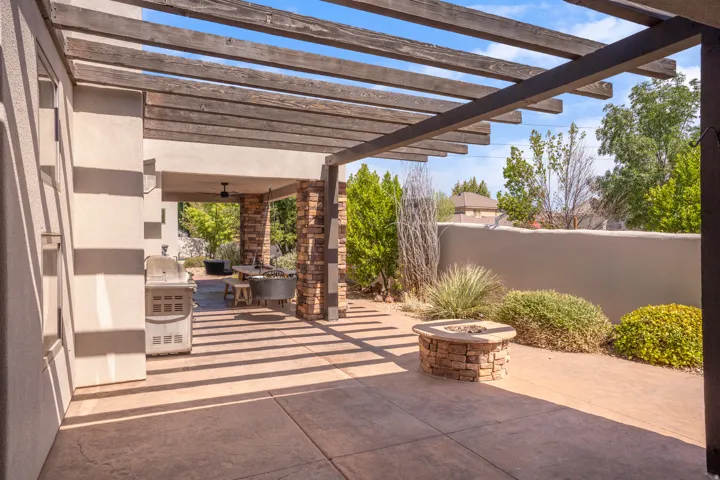 Expansive outdoor patio featuring a wooden pergola, concrete flooring, and a built-in stone fire pit