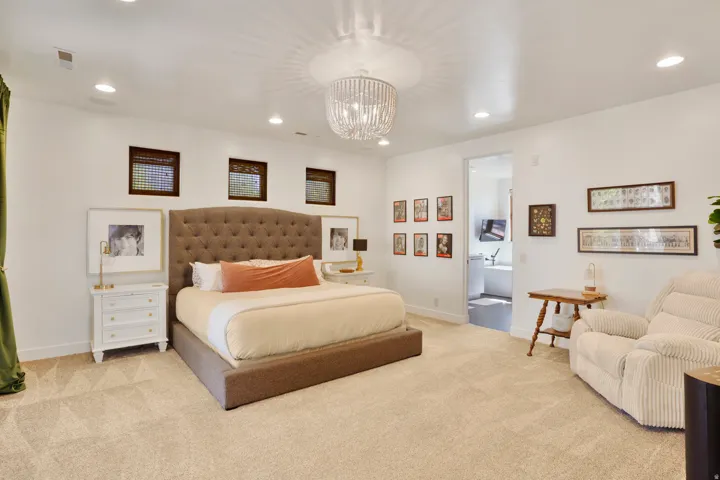 Spacious room featuring neutral carpeting, a large tufted headboard, and a contemporary chandelier