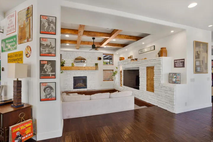 Spacious interior featuring wood-finish flooring, exposed ceiling beams, a white brick fireplace with wood mantel, a built-in media center, and recessed lighting