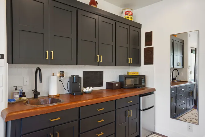 Custom kitchenette featuring dark shaker-style cabinetry with gold-tone hardware, a copper sink, and wood-finish countertops