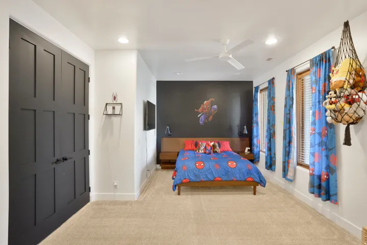 Spacious room featuring neutral carpeting, recessed lighting, a modern ceiling fan, two windows with wood-finish blinds, and a built-in wood-finish headboard