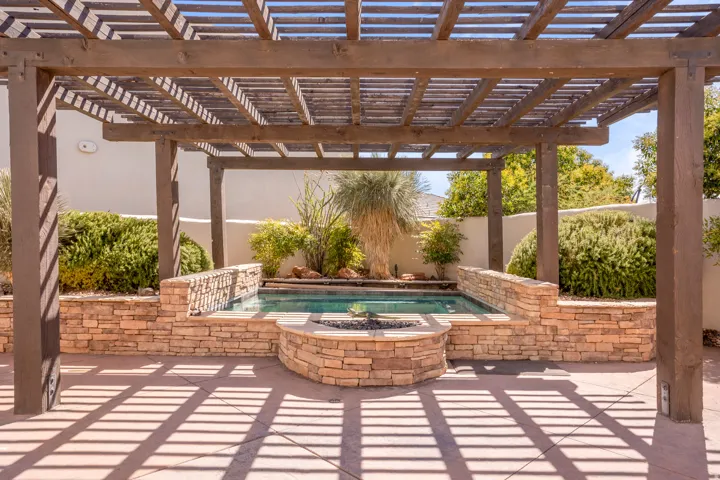 Expansive outdoor living area featuring a wooden pergola, an in-ground spa, a built-in stone fire pit, and a stone-clad retaining wall